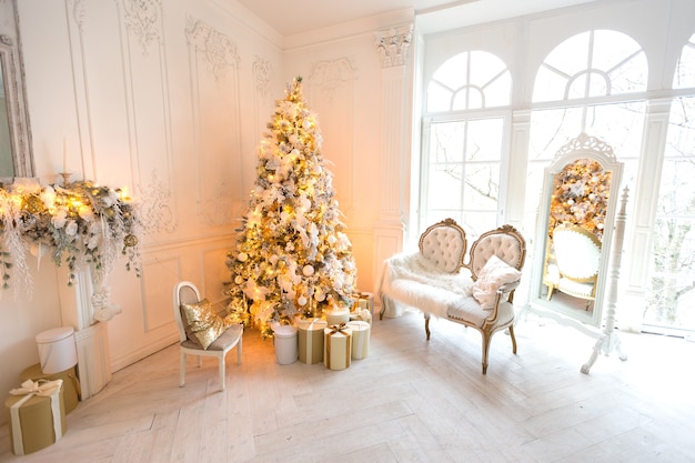 Luxurious expensive light interior living room in a royal style decorated with a Christmas tree and large windows