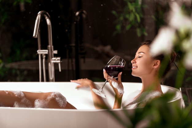 Una lussuosa ragazza si rilassa in un bagno di bolle con un bicchiere di vino. spa e relax