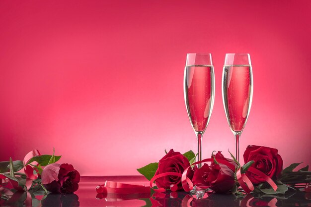 Luxurious glasses with sparkling wine surrounded by roses on a mirror surface