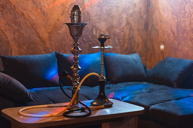 Photo luxurious hookah stands on a table next to a large sofa