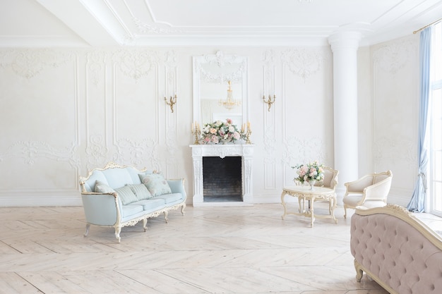 Luxurious light interior in the Baroque style. A spacious room with a road chic beautiful furniture, a fireplace and flowers. plant stucco on the walls and light wood parquet