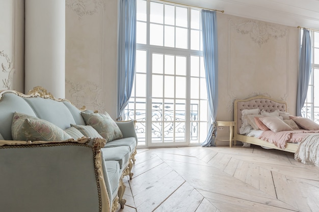 Luxurious light interior in the Baroque style. A spacious room with a road chic beautiful furniture, a fireplace and flowers. plant stucco on the walls and light wood parquet