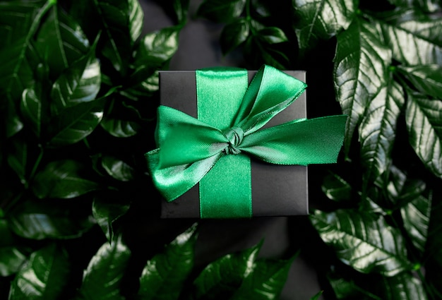 側面、フラットレイアウト、自然の概念の葉と暗い背景に緑のリボンと豪華な黒いギフトボックス。