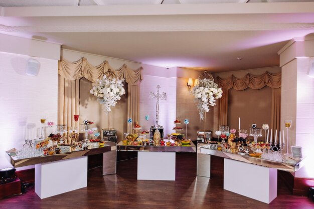 金色の結婚式の豪華なキャンディーバーお祭りのテーブルの上に立っている花で飾られたキャンディーバー