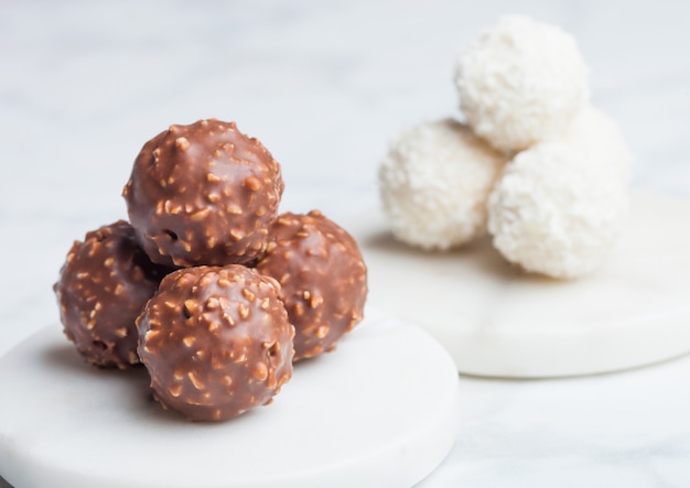Foto caramelle di lusso al cioccolato con nocciole e crema bianca con scaglie di cocco rotonde caramelle sul tavolo di marmo.