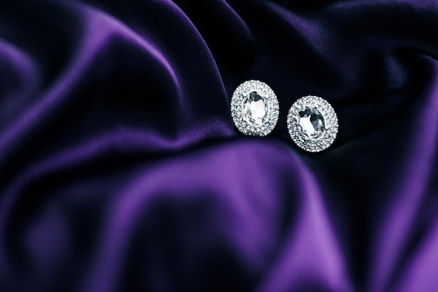 Luxury diamond earrings on dark violet silk fabric holiday glamour jewelery present