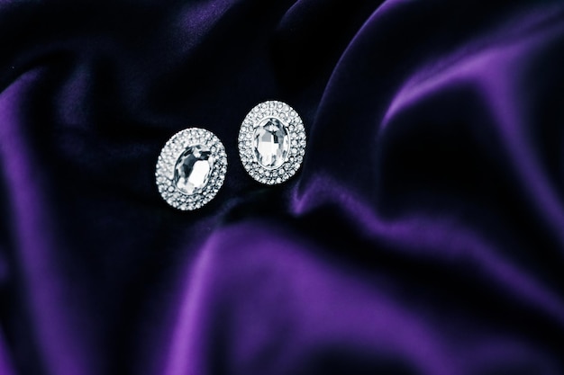 Luxury diamond earrings on dark violet silk fabric holiday glamour jewelery present