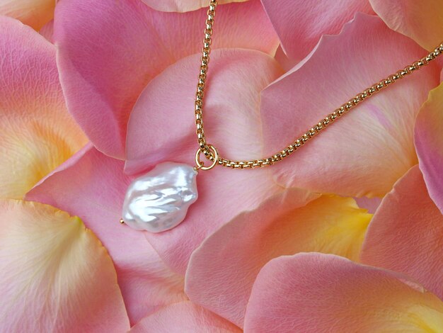 Luxury elegant baroque pearl pendant with golden chain on delicate pink yellow rose petals. Close-up shot