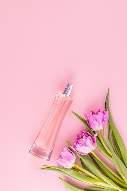Foto bottiglia di vetro di lusso di profumo o spray cosmetico femminile su sfondo rosa con fiori primaverili concetto di profumo e bellezza vista verticale