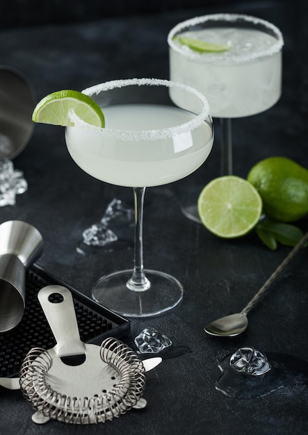 Photo luxury glasses of margarita cocktail with fresh limes and bar mat with strainer and jigger