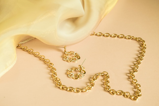 Luxury gold jewelry chain and earrings on pink background with silk