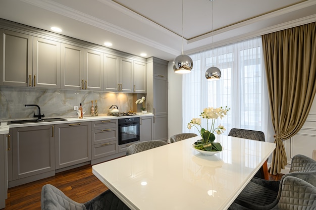 Роскошный серый и белый современный классический интерьер кухни с обеденным столом выполнен в современном стиле