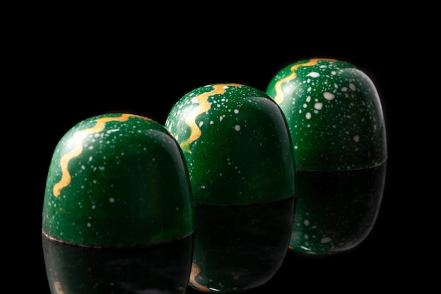 Роскошные шоколадные конфеты ручной работы на черном фоне Зеленые конфеты с разноцветными каплями Концепция продукта для шоколатье