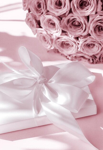 Foto confezione regalo di lusso in seta per vacanze e bouquet di rose su sfondo rosa cipria sorpresa romantica e fiori come regalo di compleanno o di san valentino