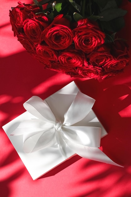 Confezione regalo di lusso in seta per vacanze e bouquet di rose su sfondo rosso sorpresa romantica e fiori come regalo di compleanno o di san valentino