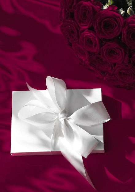 Confezione regalo di lusso in seta per vacanze e bouquet di rose su sfondo vino sorpresa romantica e fiori come regalo di compleanno o di san valentino