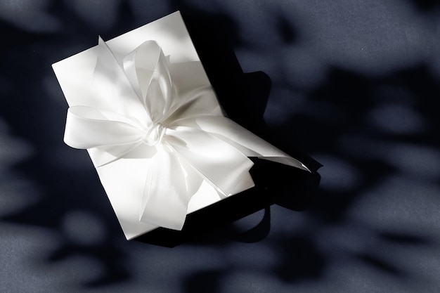 Luxury holiday white gift box with silk ribbon and bow on black background luxe wedding or birthday present