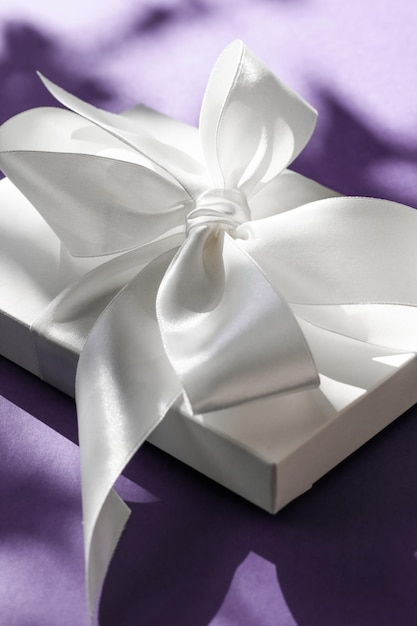 Luxury holiday white gift box with silk ribbon and bow on violet background luxe wedding or birthday present