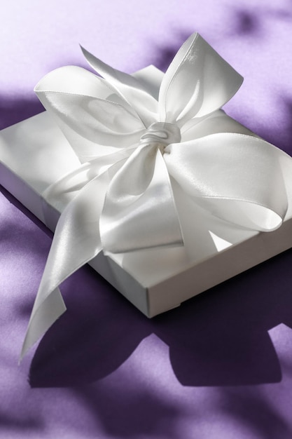 Confezione regalo bianca per vacanze di lusso con nastro di seta e fiocco su sfondo viola, matrimonio di lusso o regalo di compleanno