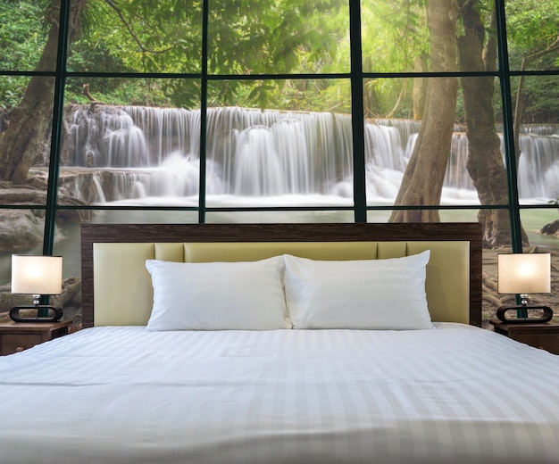 Luxury Interior bedroom with windows glass beside Beautiful waterfall in the deep forest,