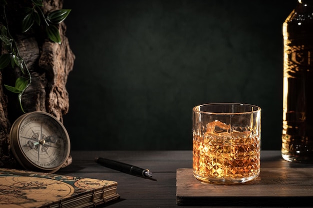 Luxury life on glass of whisky with ice and bottle on wooden table on dark background with copy space