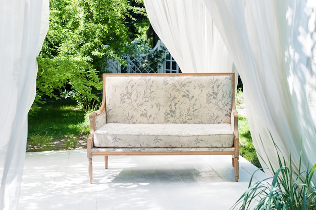 Gazebo moderno di lusso con mobili morbidi e tende all'interno del giardino. padiglione cerimonia di nozze estive.