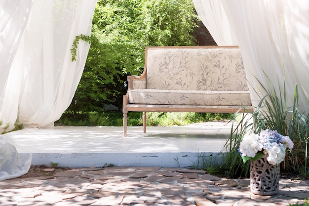 Luxury modern gazebo with soft furniture and curtains inside garden. Summer wedding ceremony pavilion.