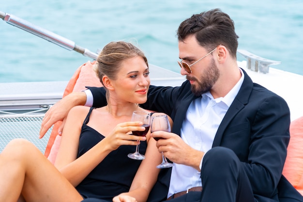 Il viaggiatore di lusso rilassante delle coppie in vestito e suite piacevoli si siede sul sacchetto del fagiolo e beve un bicchiere di vino in parte dell'yacht di crociera.