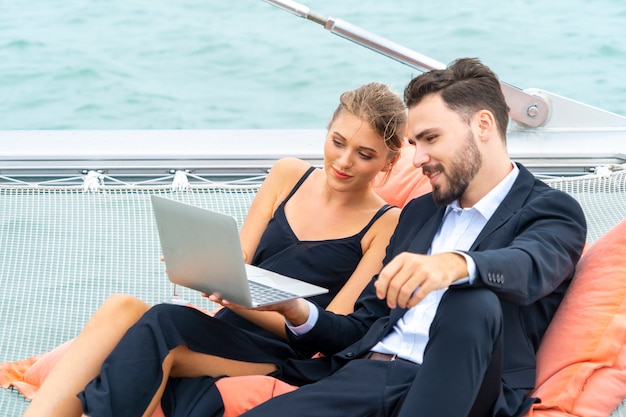 Luxury relaxing couple traveler in nice dress and suite sit on bean bag and look at computer 