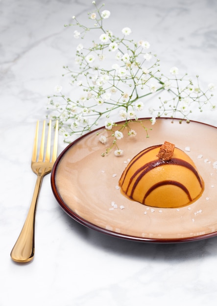 Luxury restaurant caramel dessert on plate with golden fork and flowers