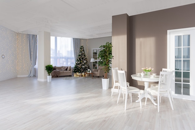 明るい色の豪華で豊かな高価なアパートのインテリア。スタイリッシュで現代的なミニマルなデザイン。太陽の光でいっぱい。クリスマスツリーで飾られたたくさんのスペース
