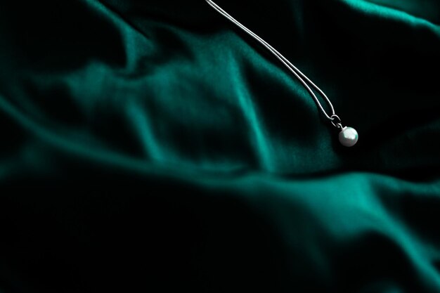 Luxury white gold pearl necklace on dark emerald green silk background holiday glamour jewelery present