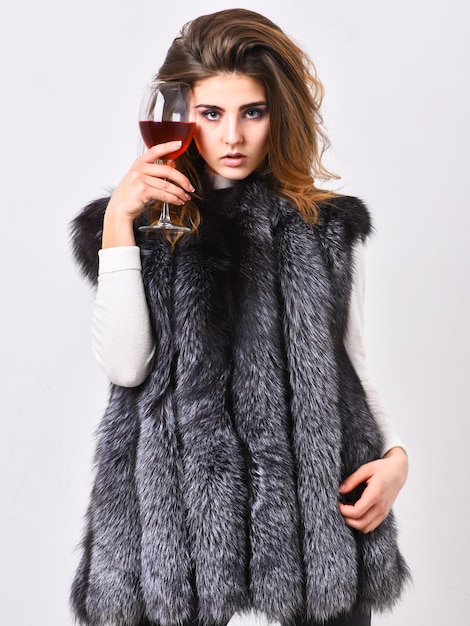 Luxury winery concept fashionable lady likes luxury fashion\
model long hair fur coat or vest hold wineglass girl enjoy luxury\
lifestyle attributes woman drink wine wear luxury fur clothing