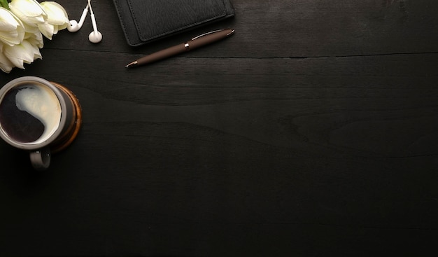 写真 黒い木製のテーブルにノートブックコーヒーカップとイヤホンのある豪華な職場上面図
