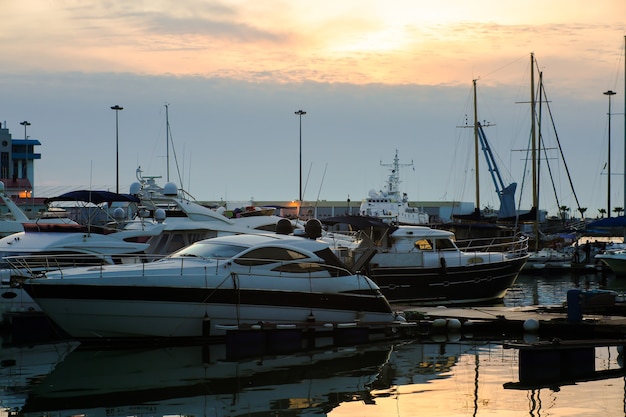 Luxury yachts docked in sea port at sunset. Marine parking of modern motor boats and blue water.