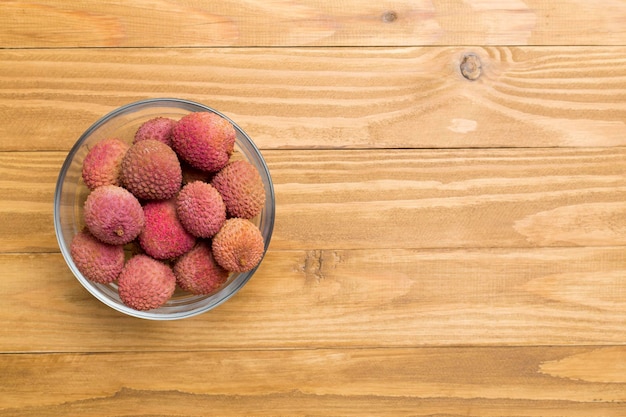 Lychee fruit in bowl on wooden background Top view copy space text