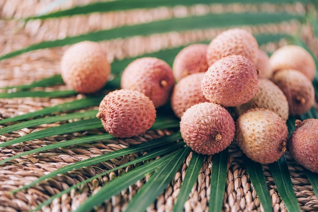 Lychee-vruchten met palmbladeren op rotanachtergrond Exotische litchi-lichee-vruchten Tropisch voedselconcept