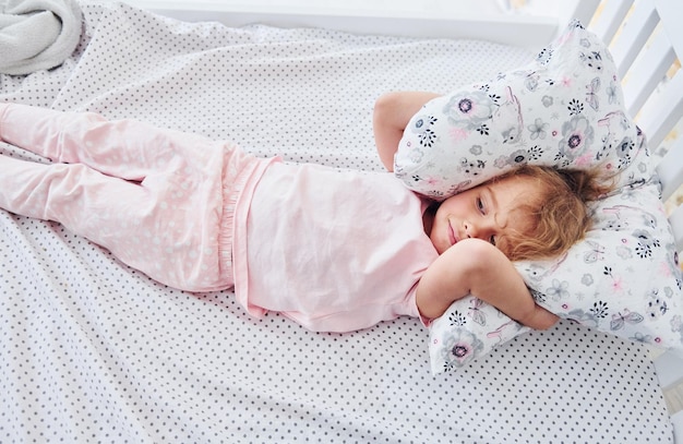 Лежа на кровати Милая маленькая девочка в повседневной одежде днем дома в помещении