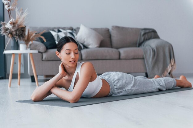 Lying down on the mat and taking a break Young woman with slim body shape in sportswear have fitness day indoors at home