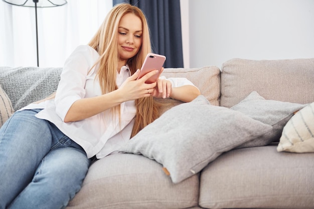 Lying down on sofa Young woman in white shirt and jeans is at home