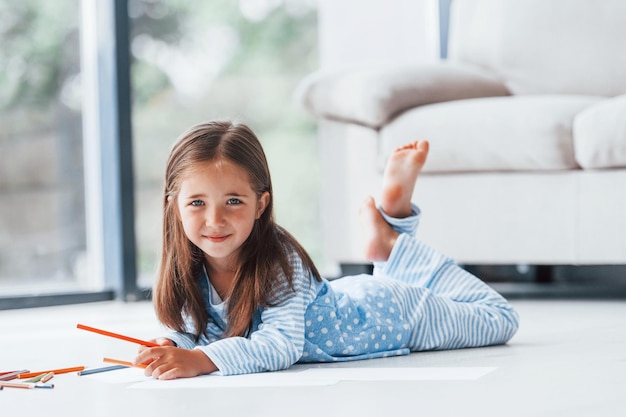 Lying on the floor and drawing Cute little girl indoors at home alone