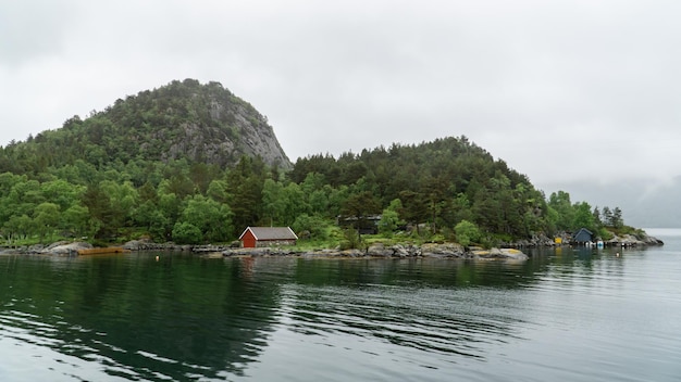 높은 산이 있는 Lysefjord 풍경 전형적인 빨간 집과 흐린 날 물에 반사