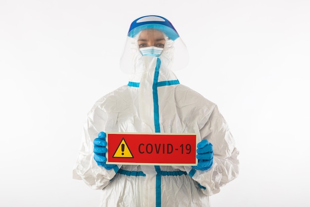 MÃ©dico enfermero con un equipo de protecciÃ³n personal y guantes de lÃ¡tex con un cartel rojo que dice: 'COVID-19'. Coronavirus, pandemia y concepto de salud.