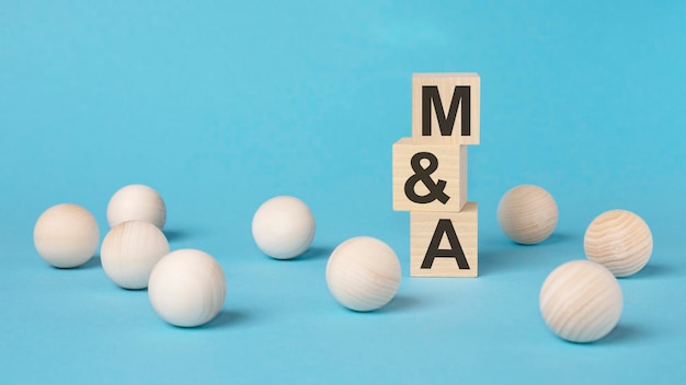 M and A Mergers and Acquisitions text on wooden block with bright blue background