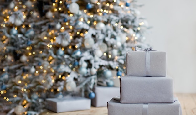 Maak grijze kerstdozen met strik bij de kerstboom met zilveren en blauwe versieringen en lichtjes