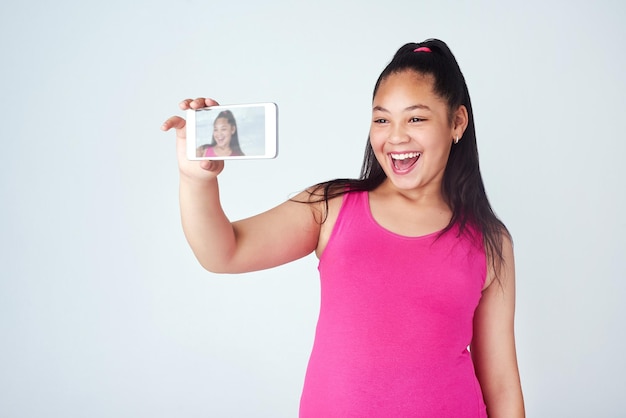 Maak je dag net zo geweldig als je selfie Studio-opname van een schattig jong meisje dat een selfie maakt met een mobiele telefoon tegen een grijze achtergrond
