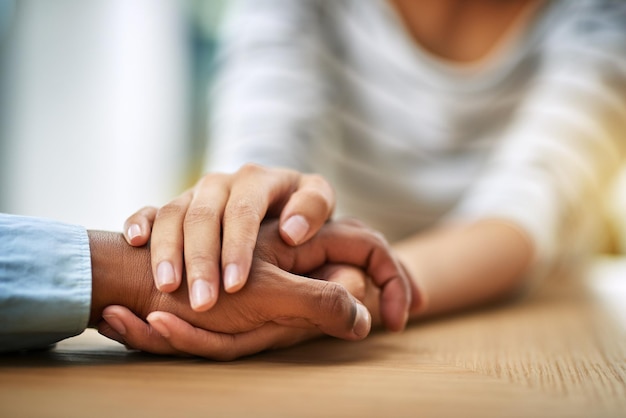 Maak je geen zorgen, ik ben hier voor jou Bijgesneden opname van twee onherkenbare mensen die elkaars hand vasthouden terwijl ze overdag aan een tafel binnen zitten