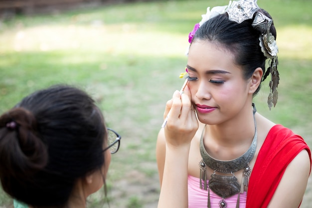 Maak omhoog kunstenaar die eyeliner vormen aan Thaise vrouw die Thaise traditionele kleding draagt