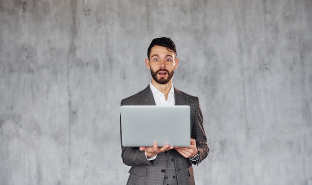 Maakt gebruik van laptop Jonge stijlvolle zakenman in pak binnenshuis Conceptie van succes