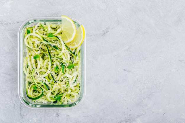 Maaltijd prep lunchbox containers Spiraalvormige courgette noedels pasta met munt, citroen en Parmezaanse kaas op grijze stenen achtergrond